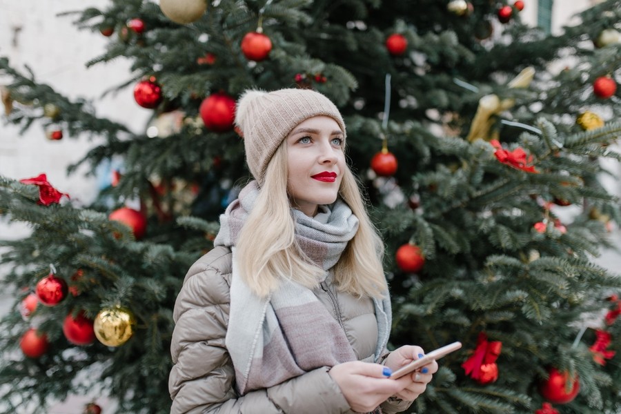 Closeup of a woman using her smartphone and smiling. Christmas tree in the background.