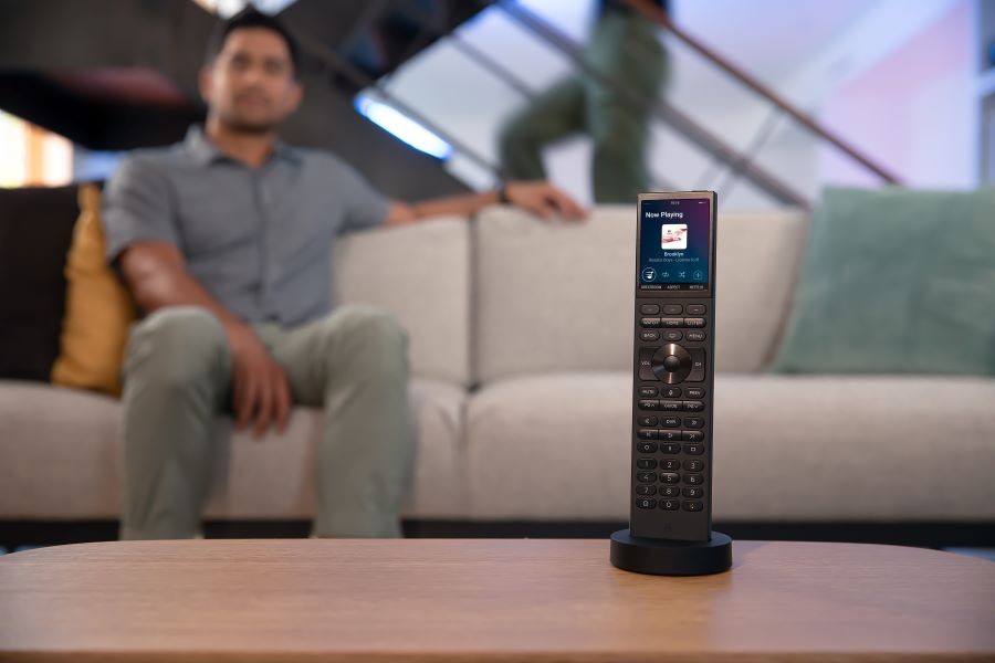 The new Halo remote is sitting on a table. A man sits on a couch in the background.