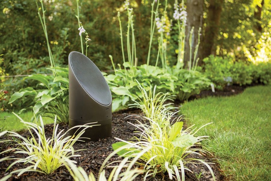 A Coastal Source 3-Way Ellipse Bollard speaker installed amid shrubs and landscape.