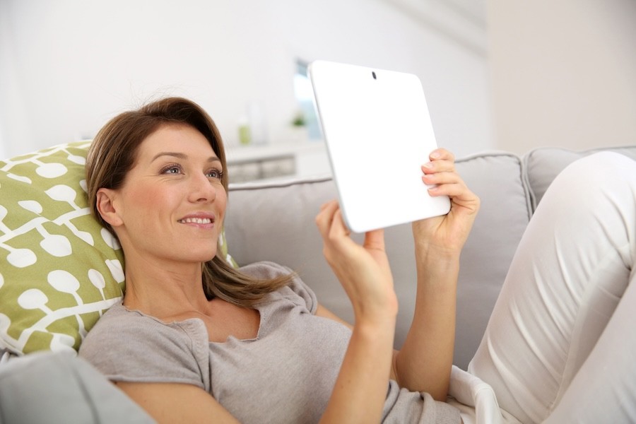 A woman relaxing on a couch while using a tablet.