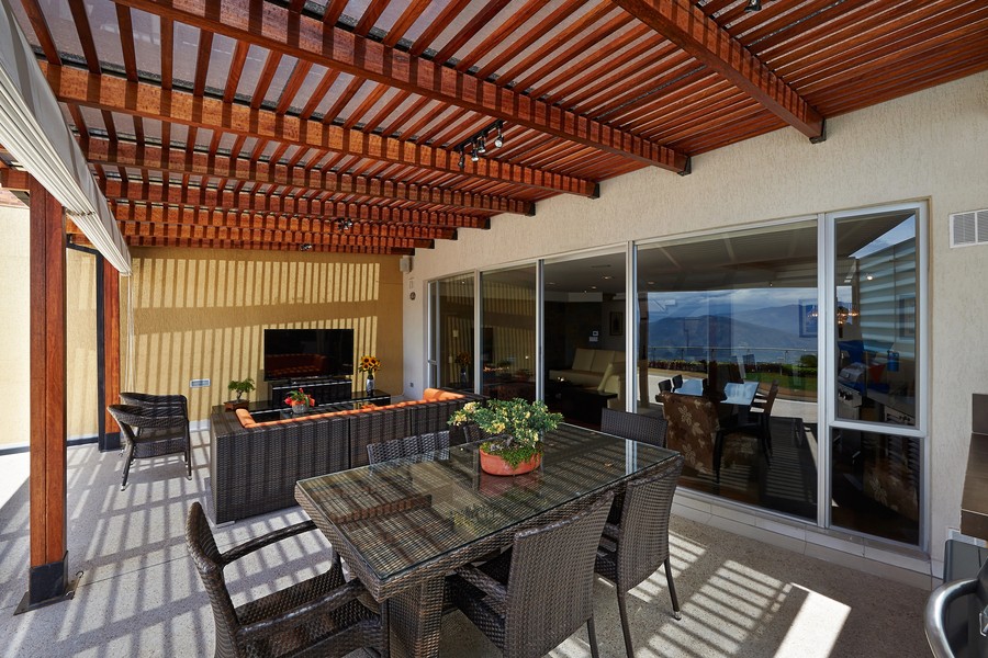 Outdoor patio with wood pergola, wicker furniture, TV, and retractable screen, designed for shade and comfort while maintaining views and indoor-outdoor flow.