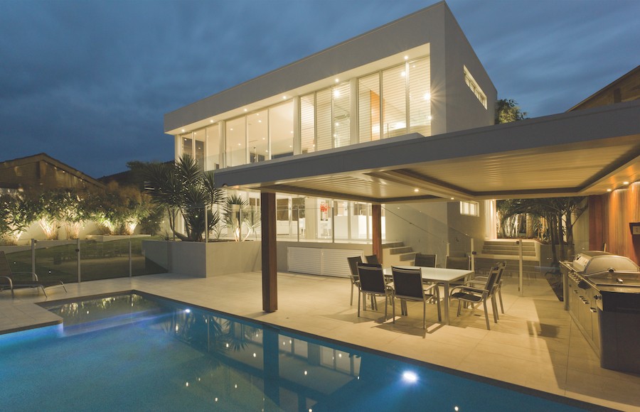 Nighttime view of home with pool and outdoor kitchen area